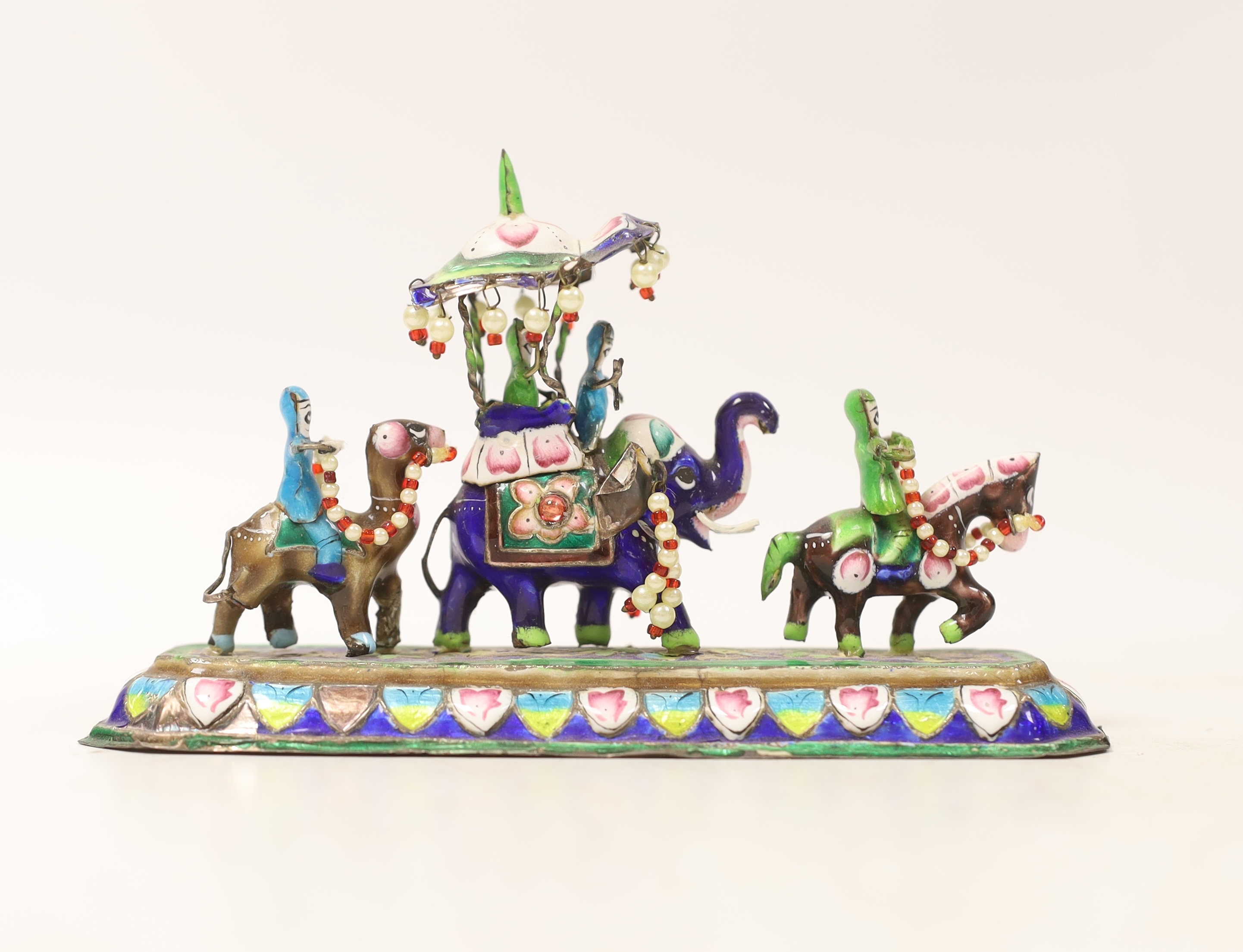 An Indian enamelled white metal model of an elephant parade, with a stamped floral decorated base, stamped ‘silver’, 15cm long